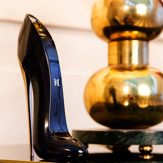 Black high-heeled shoe with a blue heel next to a gold decorative object on a white surface.